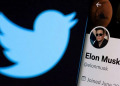 Akun twitter Elon Musk terlihat pada smartphone di depan logo Twitter, Jumat (15/4/2022).